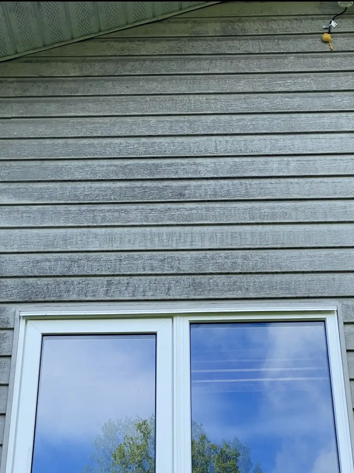 Before: pale vinyl siding streaked with algae and dirt above a white-framed window